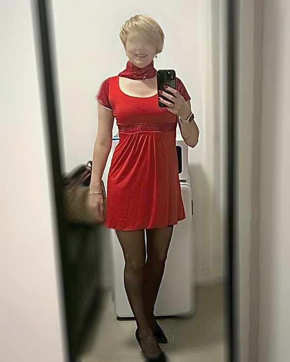 Nina, de cuerpo entero con vestido rojo de manga corta y medias negras, haciendose un selfie en el espejo de casa